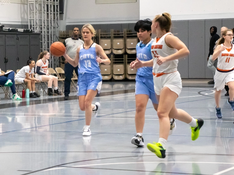 CATS Academy girls basketball players pushing the ball up the floor in Carolina blue uniforms